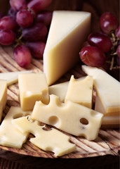 Pieces of cheese and bunches of grapes on wood illuminated with selective light