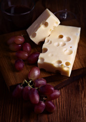 Pieces of cheese and bunches of grapes on wood illuminated with selective light