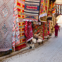 carpets on local market and walking woman in city Fes in Morocco