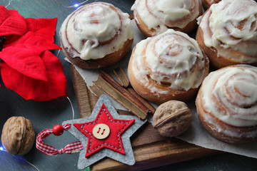 Cinnamon rolls for Christmas. Christmas cakes. Buns in glaze on a wooden table, scattered nuts and cinnamon sticks, rustic style. Homemade cake. Christmas background. Greeting card.