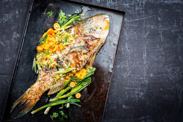 Traditional BBQ parrotfish with mango salsa as top view on a black board copy space right