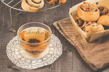 glass cup of tea and rolls with poppy in a wooden basket/glass cup of tea and rolls with poppy in a wooden basket on a dark wooden backround. Selective focus