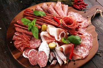 Food tray with delicious salami, pieces of sliced prosciutto crudo, sausage and basil. Meat platter with selection