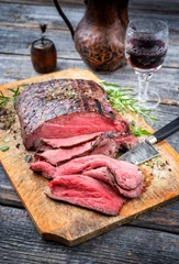 Zelfklevend Fotobehang Traditional barbecue dry aged sliced roast beef steak with herbs as closeup on an old cutting board © HLPhoto