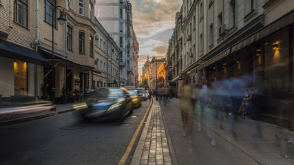 silhouettes of people,  and cars on the urban street  at sunset