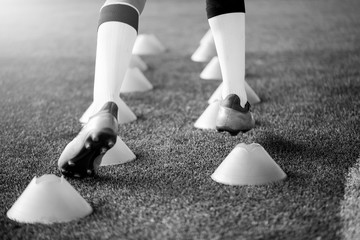 black and white picture of soccer player Jogging and jump between cone markers on artificial turf...