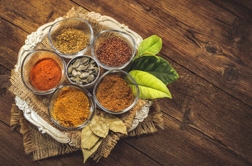 various spices in glass containers on a metal plate. kari, chilli peppers, dry spices, flax seeds, pumpkin seeds. wooden table.