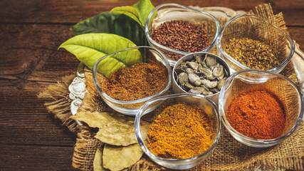 various spices in glass containers on a metal plate. kari, chilli peppers, dry spices, flax seeds, pumpkin seeds. wooden table.