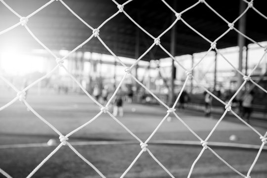 black and white picture of White mesh goal with blurry young boy soccer players sitting with coach