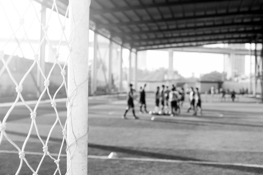 black and white picture of White mesh goal with blurry young boy soccer players sitting with coach