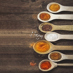 various spices in wooden spoons.on a table. kari, chilli peppers, dry spices, flax seeds, pumpkin seeds. wooden table.