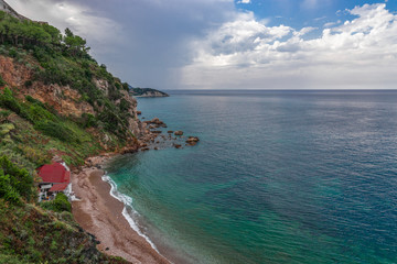 Beautiful seascape of the rocky coast and a small beach with a restaurant. Cloudy sky after rain and emerald waters of the sea of Elba island. Tuscany, Italy