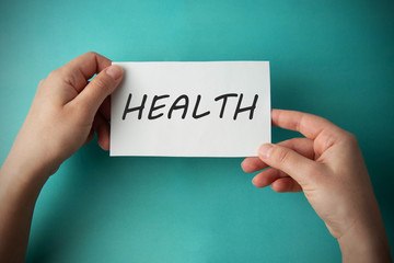 Health inscription on note. Records management. Woman's hands holding paper with Health lettering over blue background.