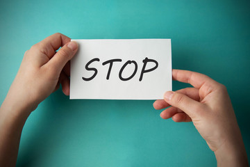 Stop inscription. Woman holding paper with STOP lettering in hands isolated on blue background.