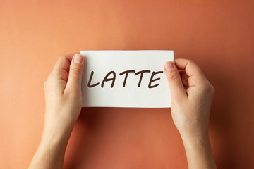 Latte inscription. Woman holding paper with Latte lettering in hands isolated brown background. Minimalist style.