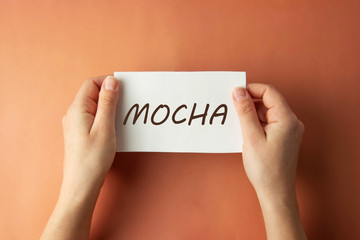 Mocha inscription. Woman holding paper with MOCHA lettering in hands isolated brown background. Top view.
