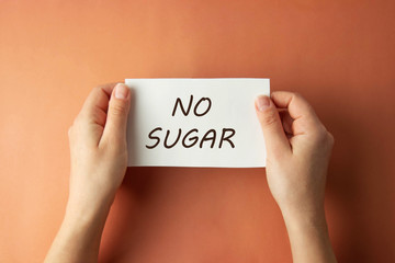 No Sugar inscription. Woman holding paper with no sugar lettering in hands isolated brown background. Top view.