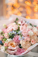 Bright bouquet of mixed flowers. Floral Bunch with blue Delphinium in glass vase. Garland bokeh on background. Christmas love