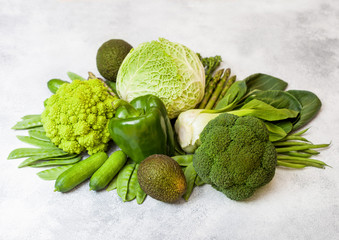Assorted green toned raw organic vegetables on white background. Avocado, cabbage, broccoli, cauliflower and cucumber with trimmed and mung beans, pak choi, loose pepper and lettuce. Green energy