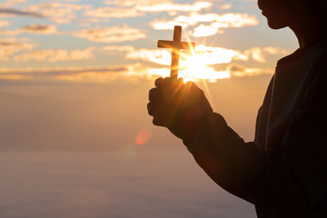 Silhouette of cross in human hand, the background is the sunrise., Concept for Christian,...