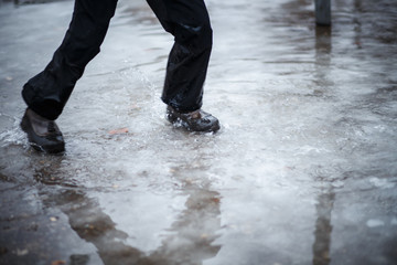 A child in snowboots boots is standing in a puddle of melted snow. Ice on the roads in the city....