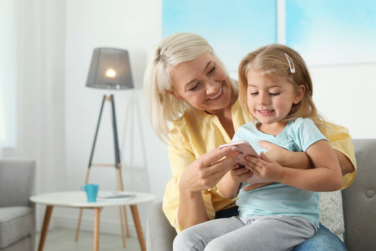 Little girl with her grandmother using smartphone at home, space for text. Family time
