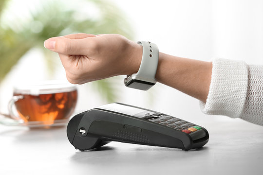 Woman using terminal for contactless payment with smart watch at table, closeup