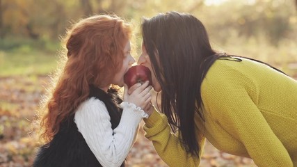 A happy mother and cute little daughter sitting together and playing with apple in a city park on a picnic. Autumn time - Powered by Adobe