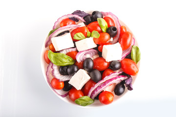 Greek salad with fresh cherry tomatoes, feta cheese, black olives, basil and onion isolated on...
