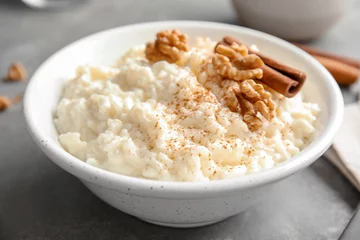 Schilderijen op glas Creamy rice pudding with cinnamon and walnuts in bowl on grey table © New Africa
