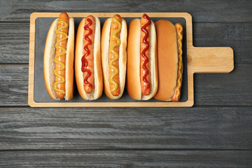 Board with hot dogs on wooden table, top view. Space for text