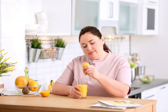 Overweight woman squeezing orange juice into glass at table in kitchen. Healthy diet