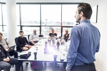 Business man making a presentation at office. Business executive delivering a presentation to his colleagues during meeting or in-house business training. Rear view. Business and entrepreneurship.