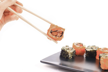 Traditional Japanese cuisine, sushi, hand holding chopsticks sushi on the background of the dish