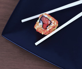 Sushi with chopsticks on a black plate on wooden background