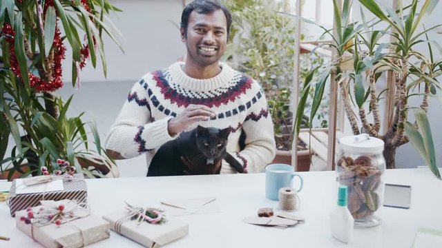 Mixed race Indian man in wool Icelandic sweater petting pet black cat or animal for relaxation in wintertime or Halloween loving favorite witch living creature which bring luck and happiness to owner