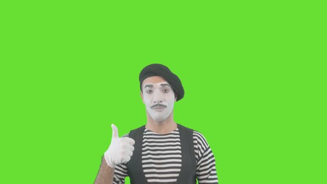Happy mime showing thumbs up. Cheerful behavior and broad smile of a male actor during the pantomime show. Isolated on green background.