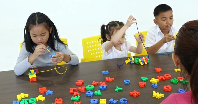 Asian teacher lets Asian student string alphabet toy together, concept for English class.