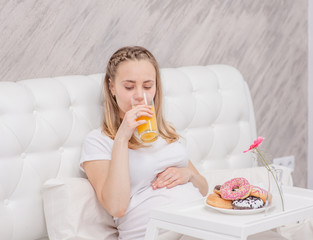 Happy pregnant woman with juice and donuts on the bed