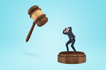 Tiny businessman about to be smashed by an inscribed gavel.