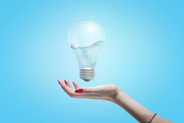 Woman's hand with open palm as if about to take hold of an electric bulb floating in the air with water inside the bulb.
