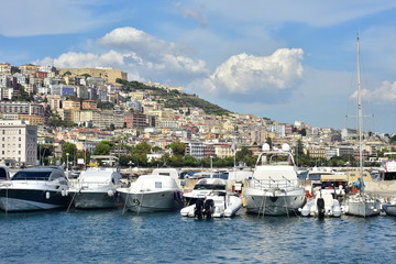 Fototapeta na wymiar Recreational vessels berthed in marina with dense urban area filled with Mediterranean style apartment buildings on hill in background on sea coast of Italy.