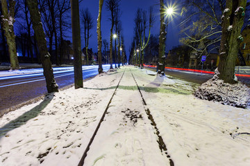 a small street of a night city with snowy tram tracks and traces of car headlights on a long exposure