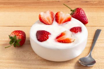 Bowl of yogurt and red fruit strawberry on the wood table. Yogurt made from milk fermented by added bacteria, often sweetened and flavored.