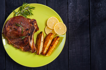 Grilled beef steak with slices of lemon and baked potatoes on a green round plate. Top view. Copy space