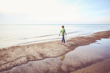Boy walking down the beach with a walking stick