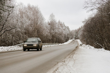 The car goes on a snowy winter road through the forest