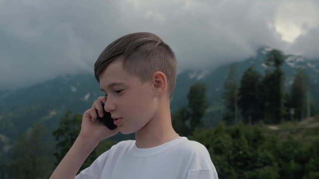 A boy talking on a smartphone while traveling against the backdrop of high mountains