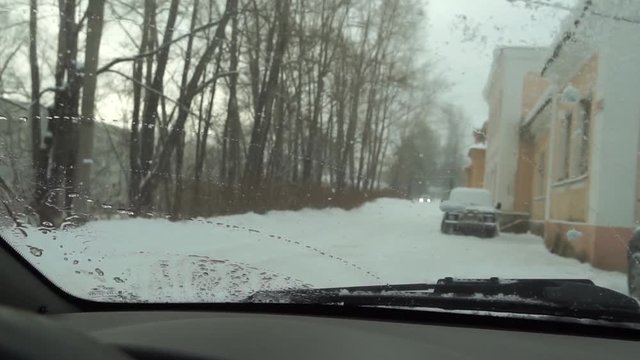 Car wipers clean the snow on the glass. The snow outside the window turns into a drop of water on the glass of the car.