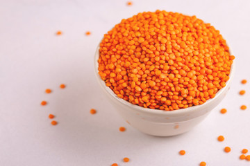 Raw red lentils in clay bowl on white marble background